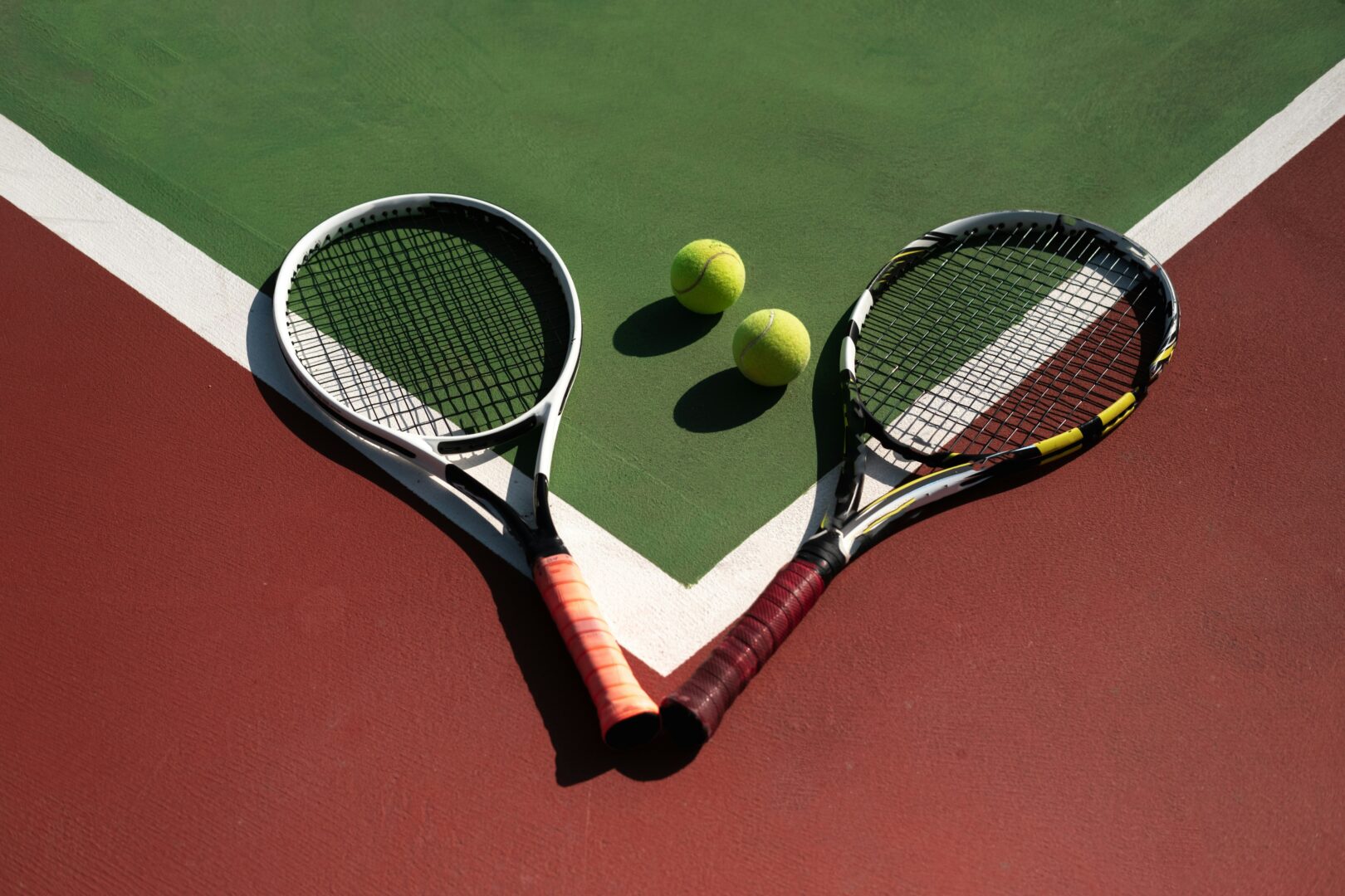 Two tennis rackets and tennis balls laying on a tennis court.