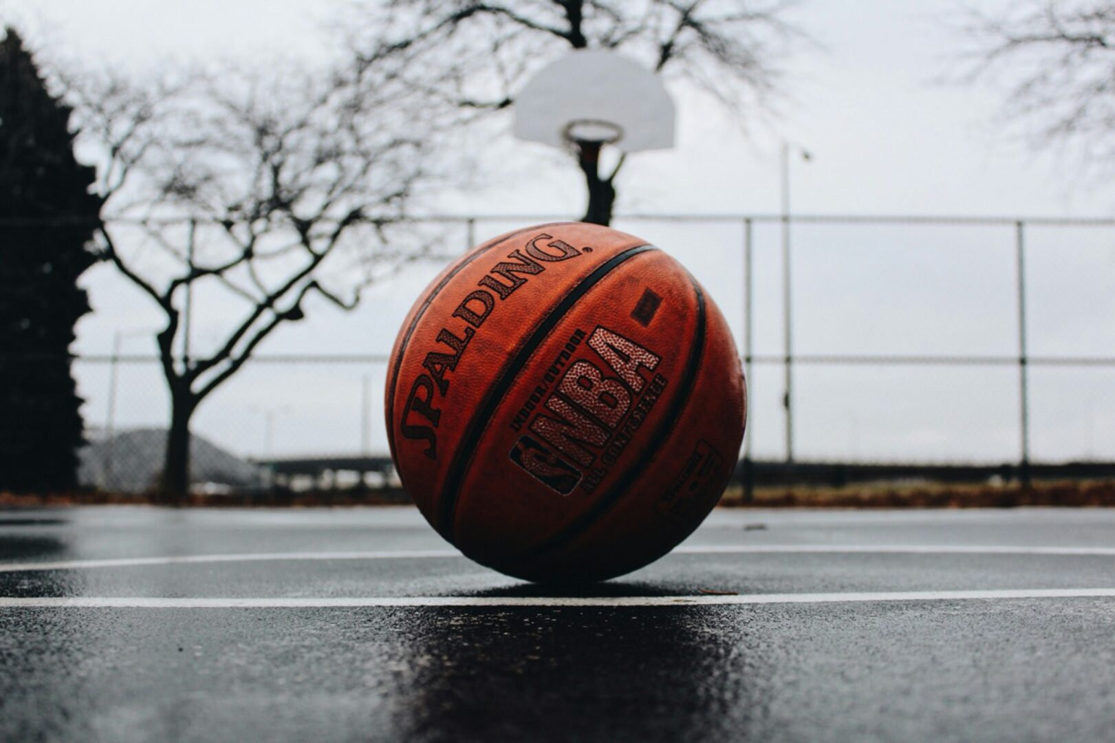 Photo of a basketball laying on a basketball court in the rain