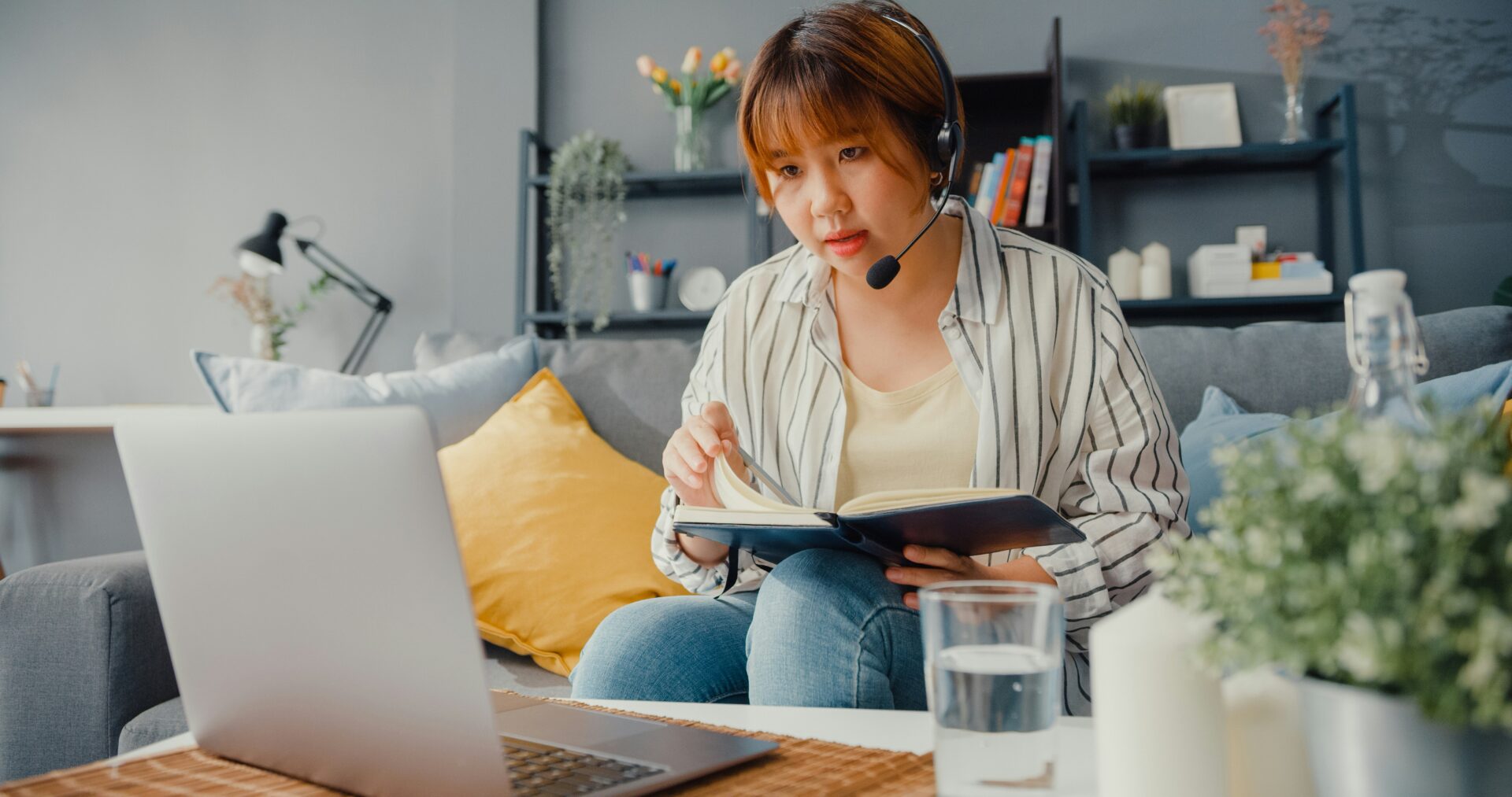 Woman sitting on her couch working on her laptop with a headset on