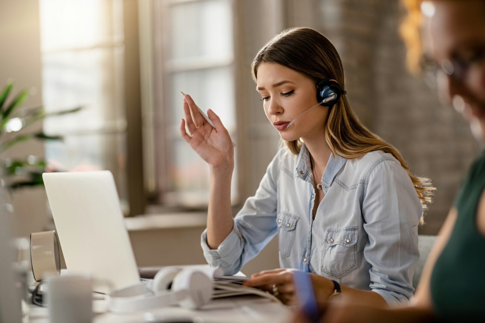A woman sitting at her desk in front of her laptop with a headset on