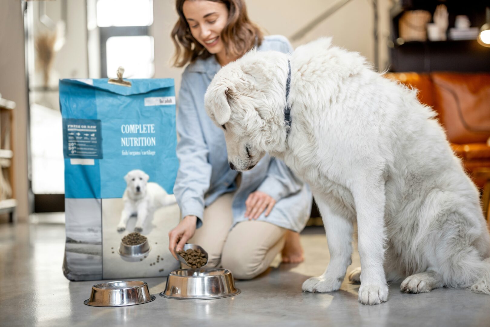 A woman putting dog food in her dog's food while he sits next to her